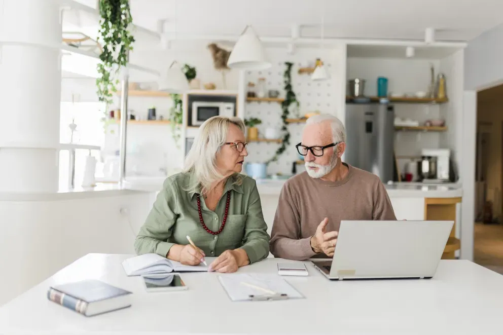Elderly couple conversing with computer and paperwork Elderly couple conversing with computer and paperwork