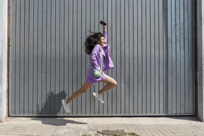 smiling woman leaping holding cell phone