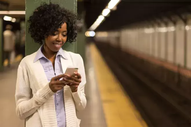 Young African American black woman in city at night texting cell phone subway station