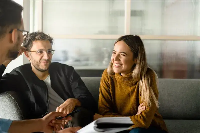 Woman smiling at man helping with paperwork, another man beside her gazing at the woman