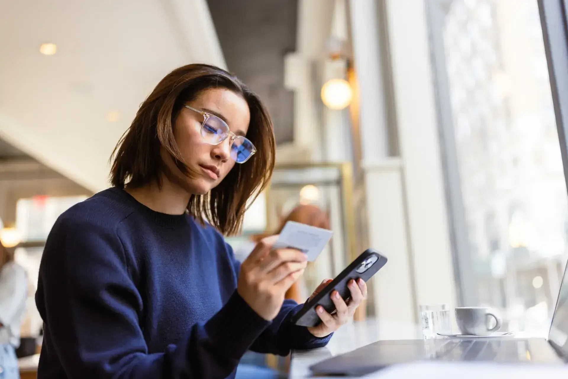 Young woman in blue sweater holding a credit card and smartphone indoors.