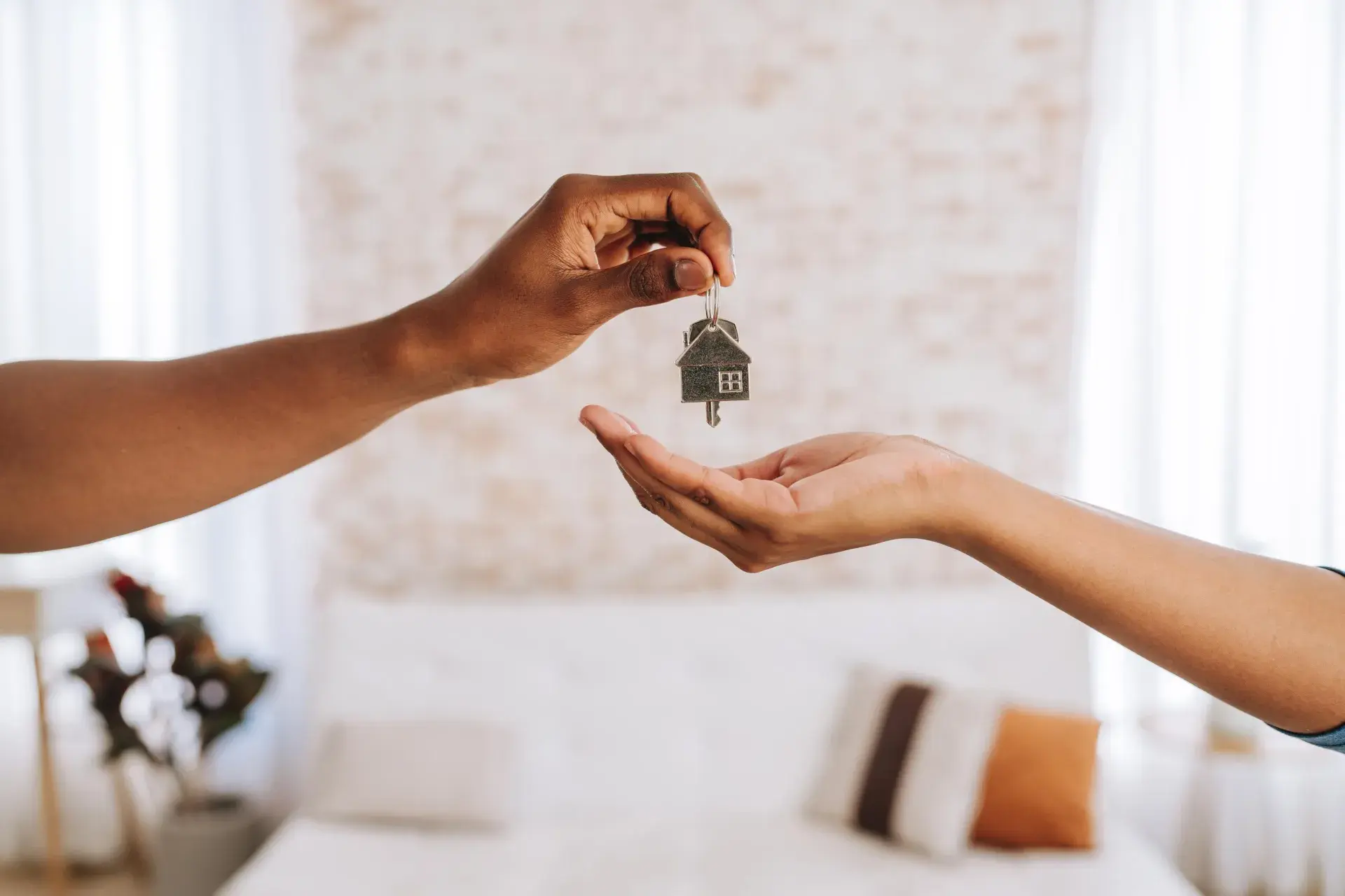 One hand is pictured delivering a set of house keys to another hand receiving.