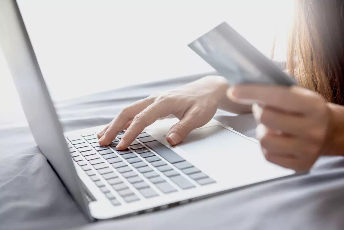Pessoa segurando um cartão e usando um laptop