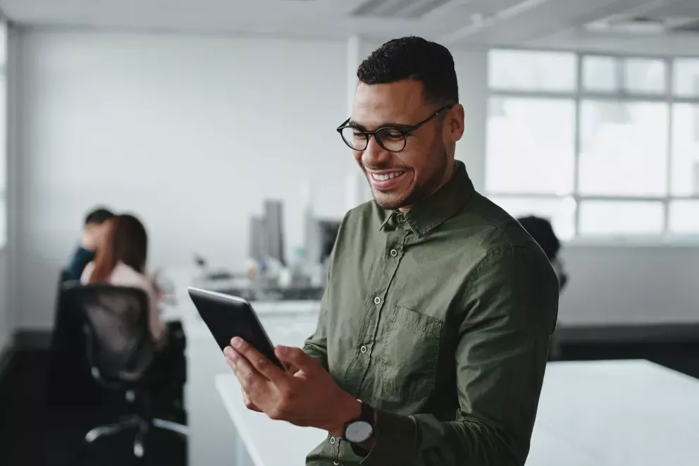 Homem feliz trabalhando em tablet no escritório Homem feliz trabalhando em tablet no escritório