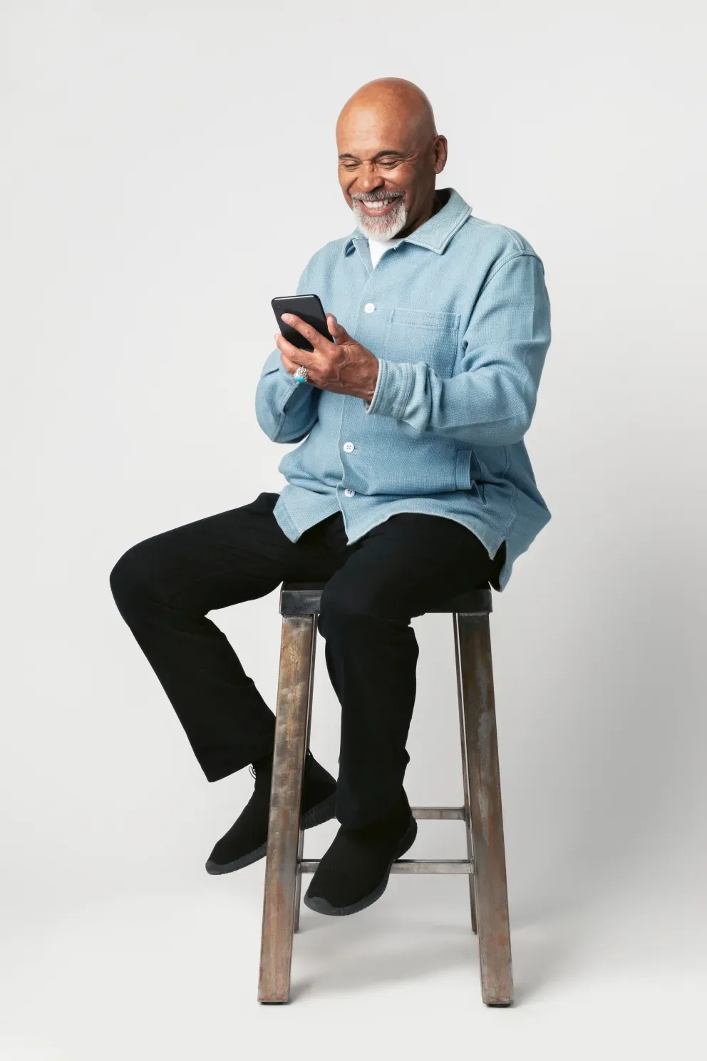 homem sênior sorridente sentado no banquinho do bar usando o telefone celular
