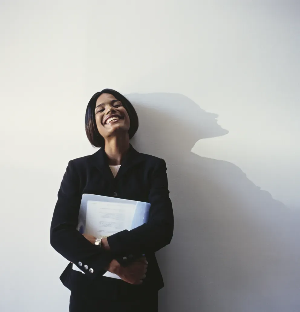 mulher de negócios sorridente encostada na parede segurando fichário