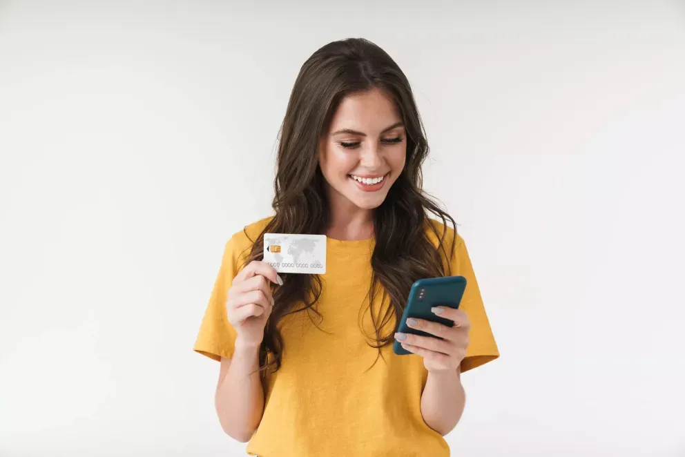 Mulher olhando para um telefone segurando um cartão de crédito