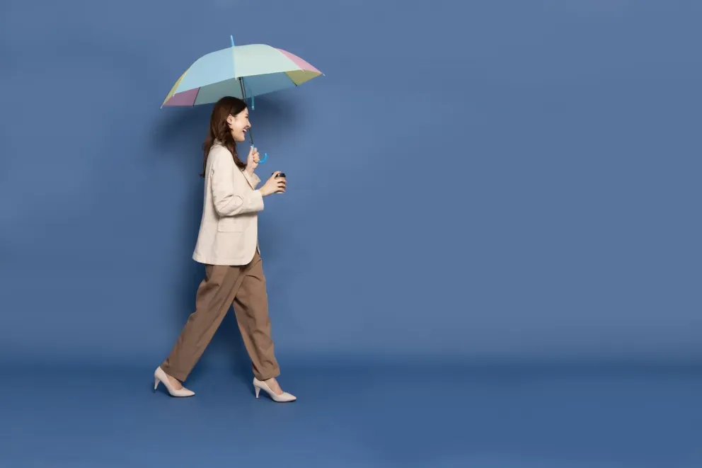 mulher de negócios sorridente caminhando segurando guarda-chuva e café