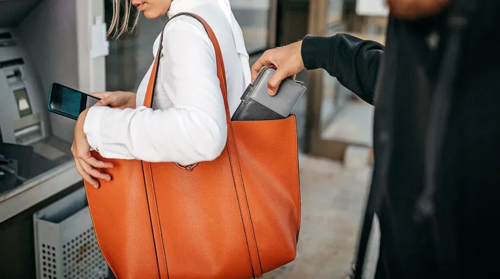 Um ladrão roubando um telefone da sacola laranja de uma mulher em um caixa eletrônico.