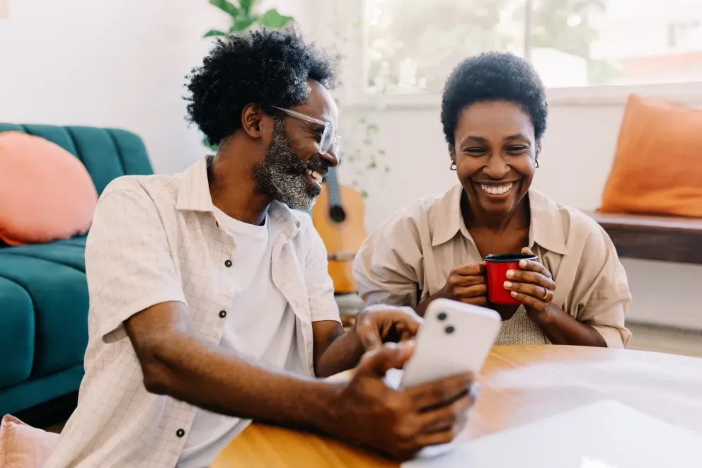 Casal sorridente compartilhando um momento olhando para um telefone juntos dentro de casa.