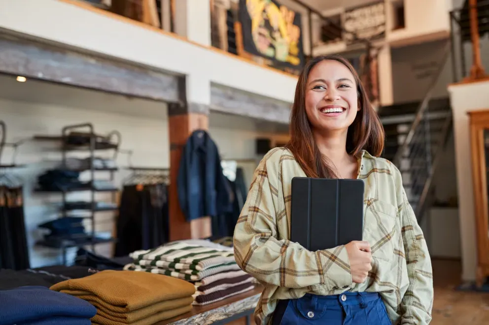 Funcionária sorridente segurando um tablet em uma loja de roupas.