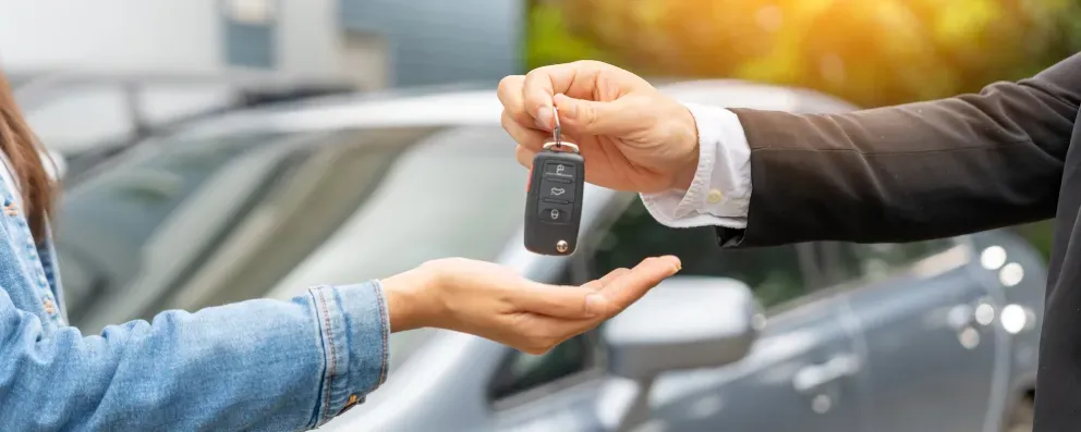 Um revendedor de carros entregando chaves para um cliente em um estacionamento.