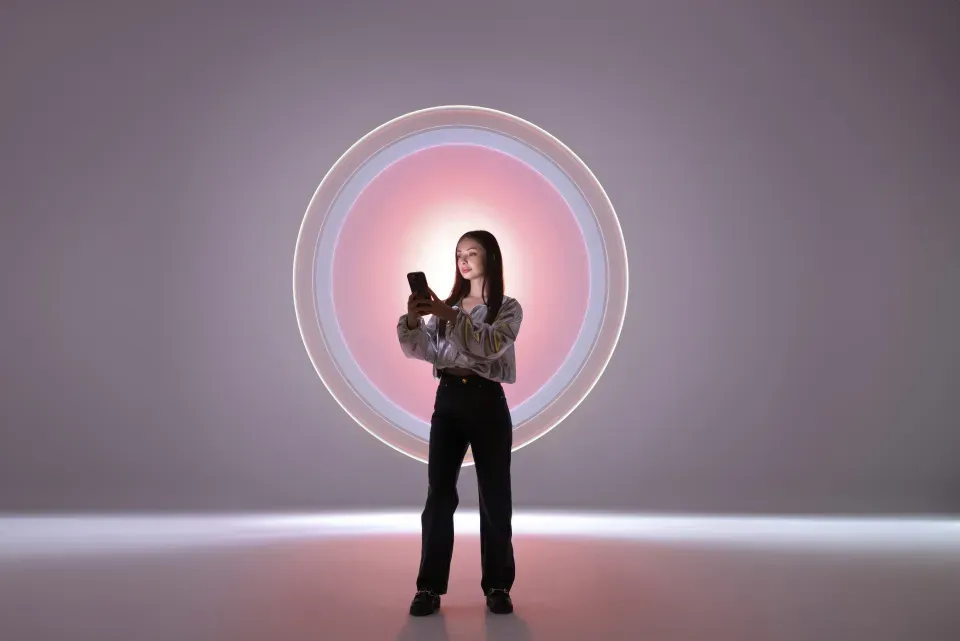 Mulher em pé na frente de uma grande instalação de luz circular rosa e branca brilhante.