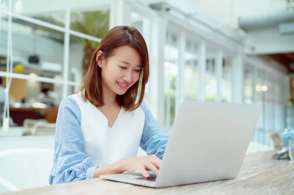 Jovem mulher asiática sorrindo enquanto usava um laptop em uma mesa de café ao ar livre. Jovem mulher asiática sorrindo enquanto usava um laptop em uma mesa de café ao ar livre.