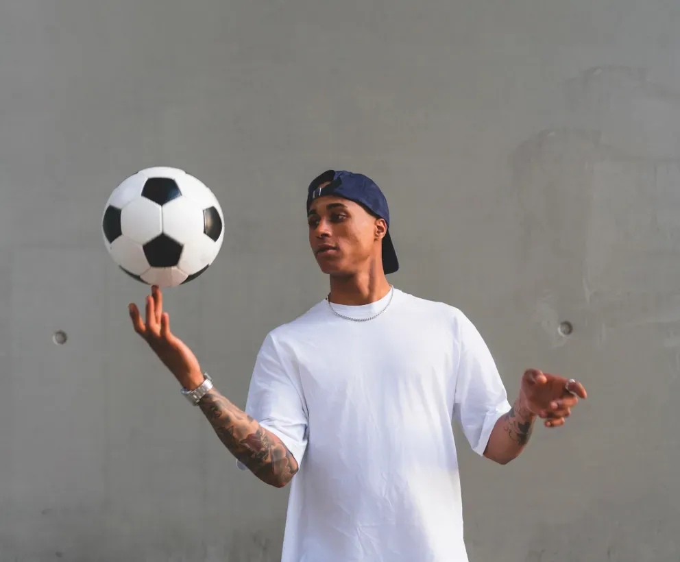 Homem de camiseta branca equilibrando uma bola de futebol em um dedo ao ar livre. Homem de camiseta branca equilibrando uma bola de futebol em um dedo ao ar livre.