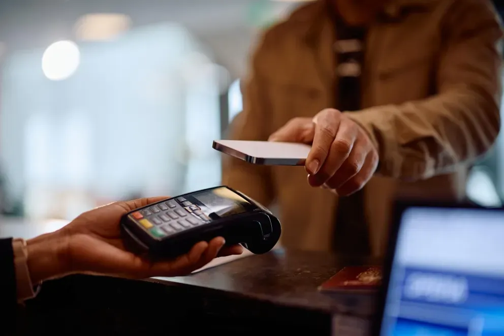 Customer paying by tapping a contactless card on a handheld card reader held by another person.