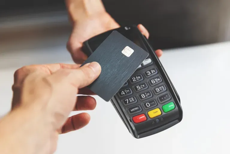 Person's hand inserting credit card into black payment terminal with colorful buttons