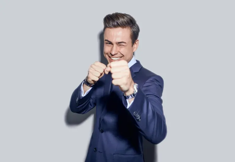 Homem de terno azul sorrindo e posando com os punhos erguidos contra um fundo cinza. Homem de terno azul sorrindo e posando com os punhos erguidos contra um fundo cinza.