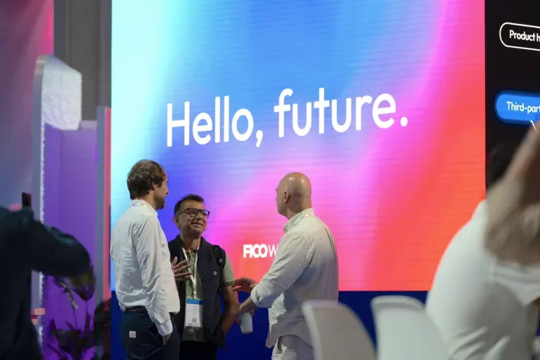 Three people conversing at a tech conference in front of a large screen displaying "Hello, future."