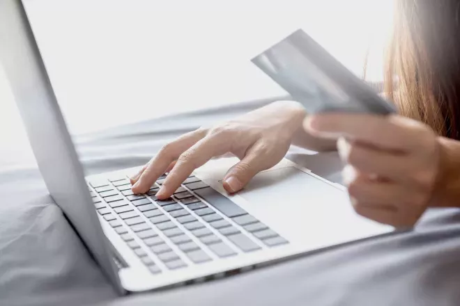 Pessoa segurando um cartão e usando um laptop