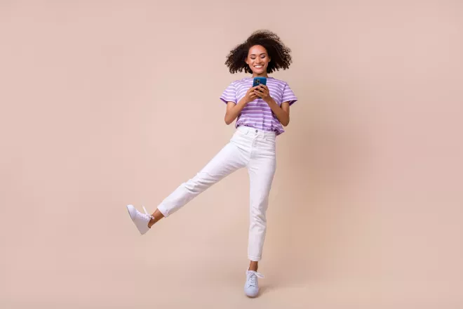 Mulher sorridente pulando com celular na mão Mulher sorridente pulando com celular na mão