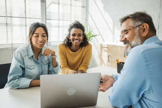 Três profissionais tendo uma reunião de negócios amigável em uma mesa branca com laptop e documentos. Três profissionais tendo uma reunião de negócios amigável em uma mesa branca com laptop e documentos.