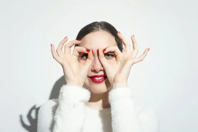 a woman with her fingers in the shape of circles over each of her eyes a woman with her fingers in the shape of circles over each of her eyes