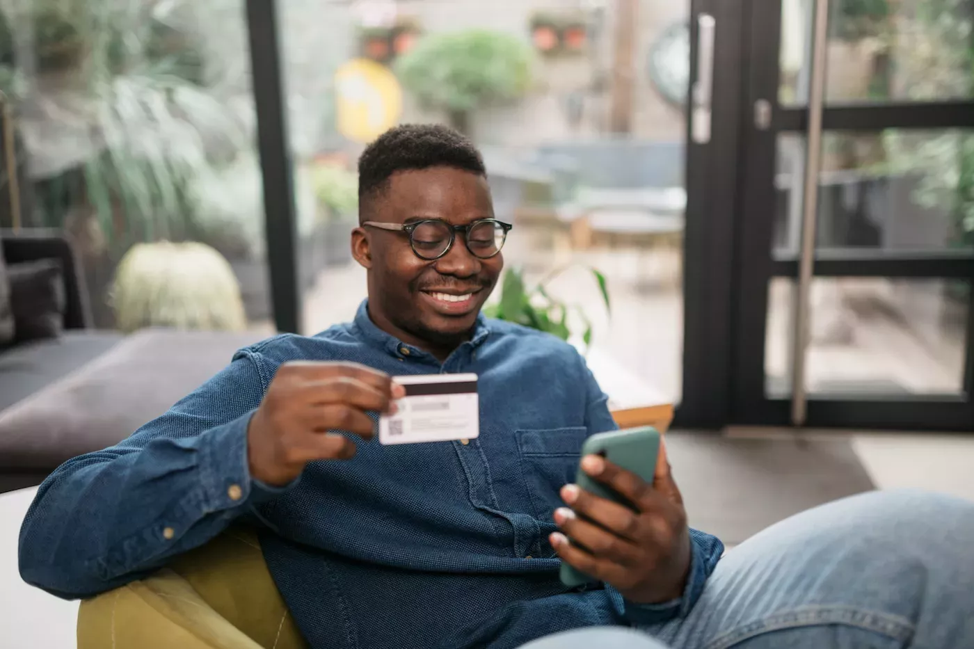 Homem olhando para um celular e segurando um cartão de crédito