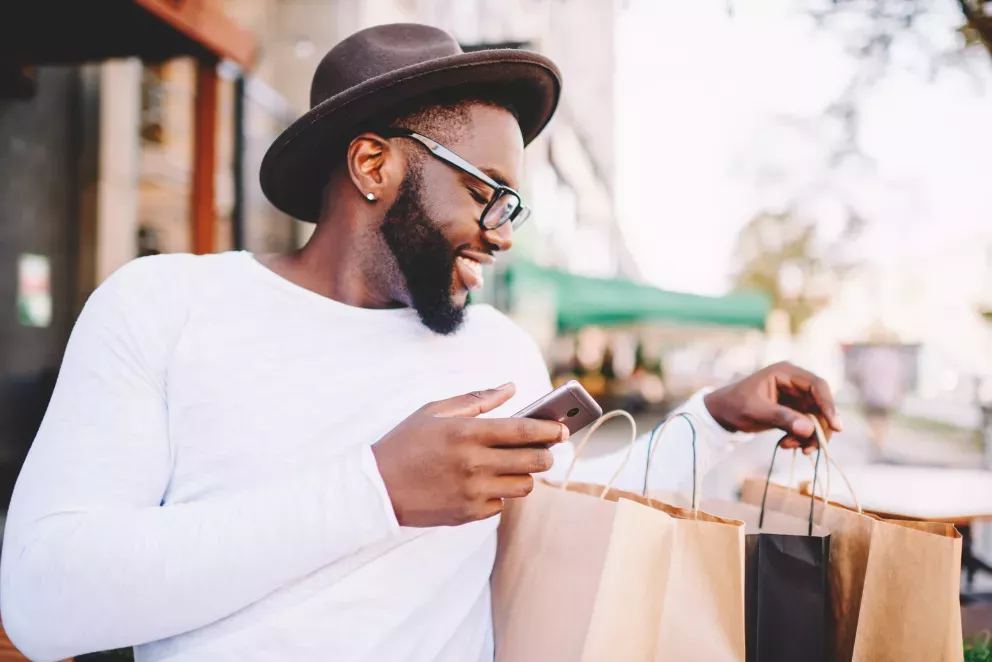 Lächelnder Mann, der Einkaufstüten durchsucht und sein Handy benutzt