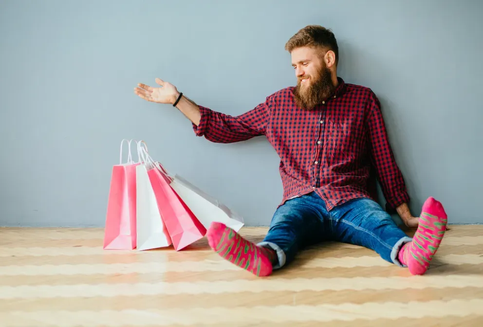 Mann in Socken sitzt mit Einkaufstüten