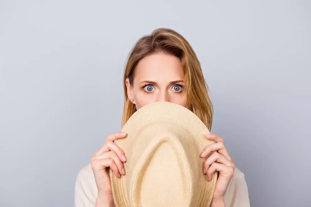 Frau mit schockiertem Gesichtsausdruck, die sich hinter Hut versteckt