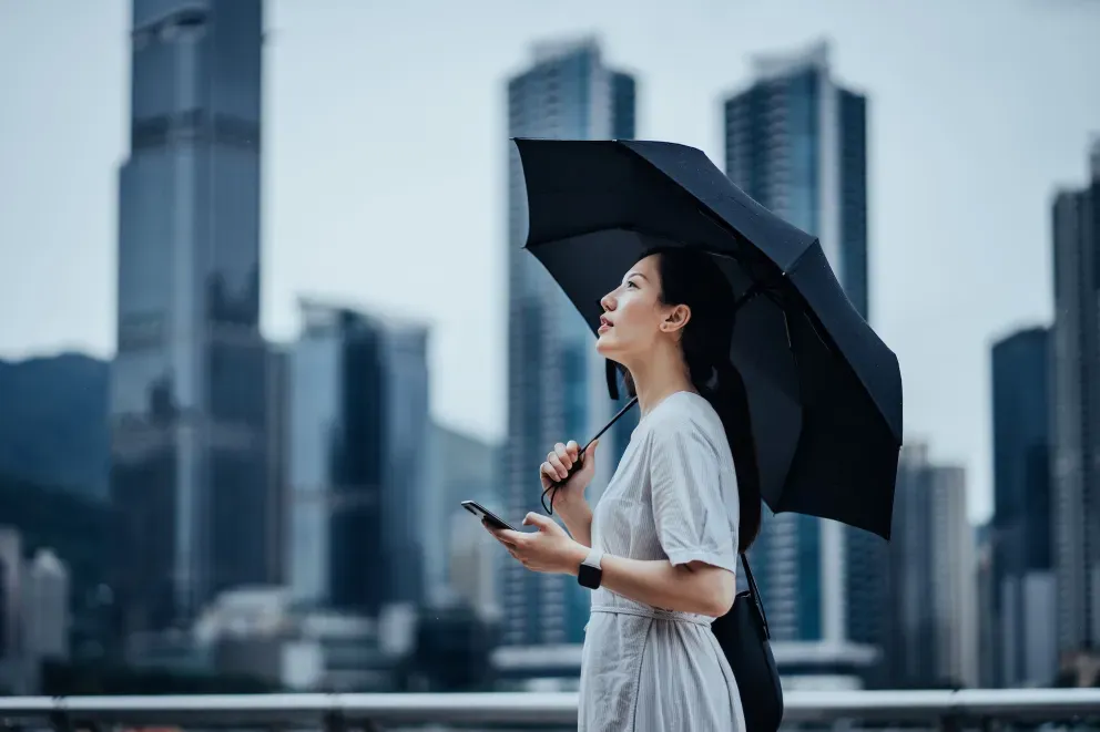 Frau mit Regenschirm und Telefon in der Stadt