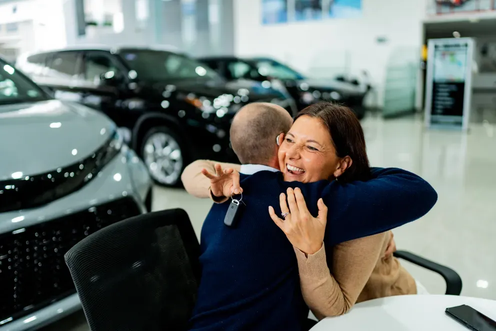 Happy couple embracing at a car dealership, woman holding car keys.