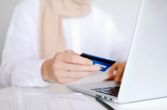 Nahaufnahme einer Person, die beim Einkaufen auf dem Laptop eine Kreditkarte in einer Hand hält Nahaufnahme einer Person, die beim Einkaufen auf dem Laptop eine Kreditkarte in einer Hand hält