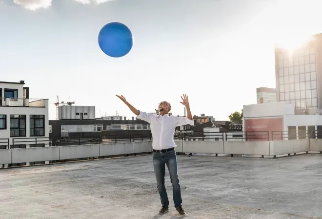 business man smiling and tossing a large ball up in the air