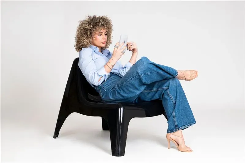 Frau sitzt im Schneidersitz auf einem Stuhl und liest Handy Frau sitzt im Schneidersitz auf einem Stuhl und liest Handy