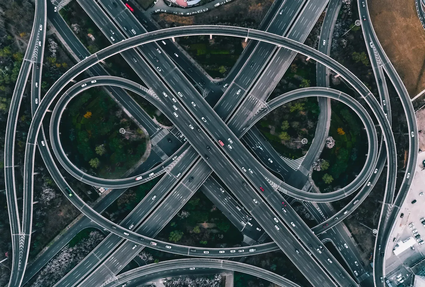 Aerial view of a complex multilevel highway interchange with looping ramps and cars, surrounded by greenery. Aerial view of a complex multilevel highway interchange with looping ramps and cars, surrounded by greenery.