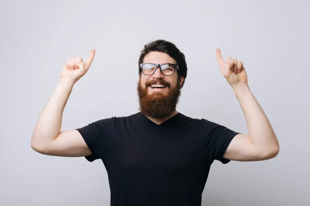 hombre sonriente señalando hacia arriba con ambas manos