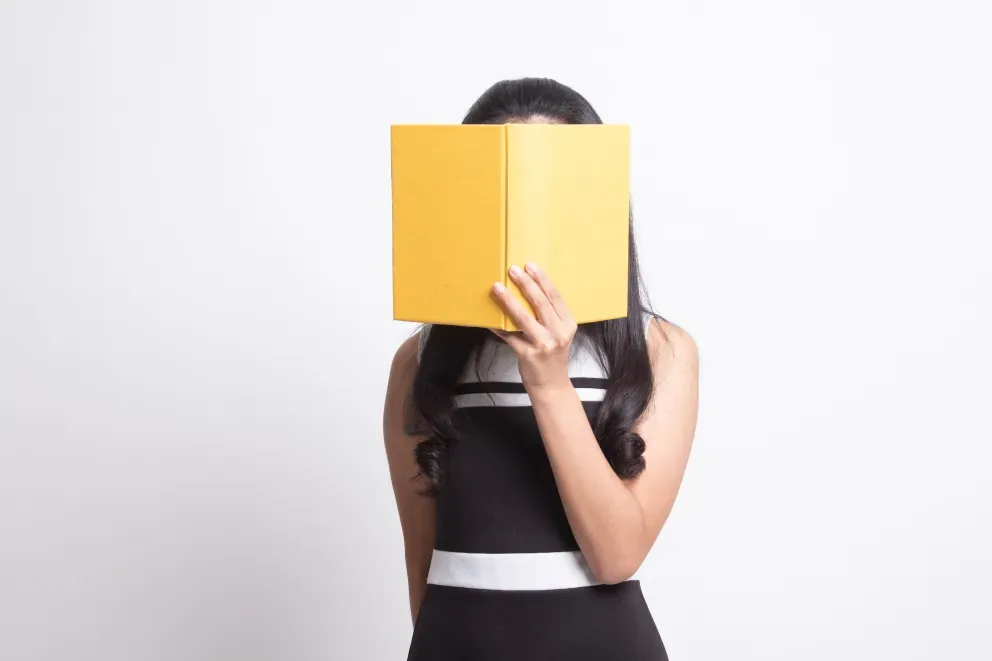 persona cubriendo la cara con un gran libro amarillo