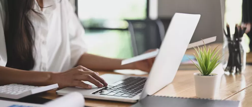 Imagen recortada de las manos de una mujer trabajando con una computadora portátil sobre un escritorio de madera