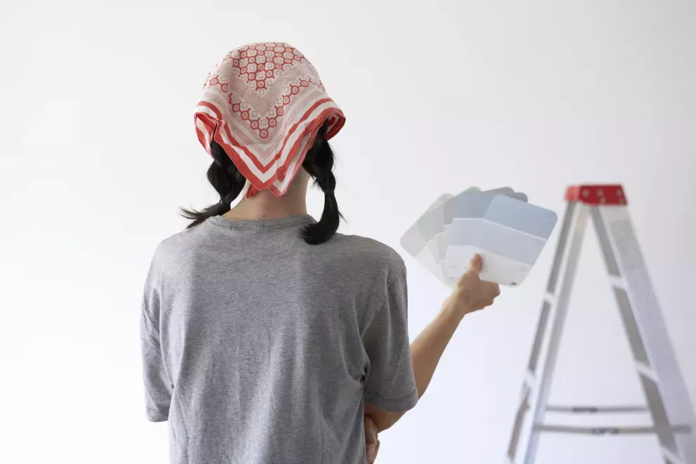 Mujer mirando una pared en blanco sosteniendo muestras de pintura
