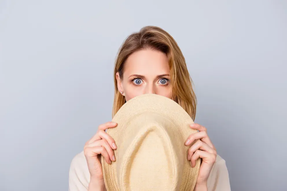Mujer con expresión de sorpresa escondida detrás de un sombrero