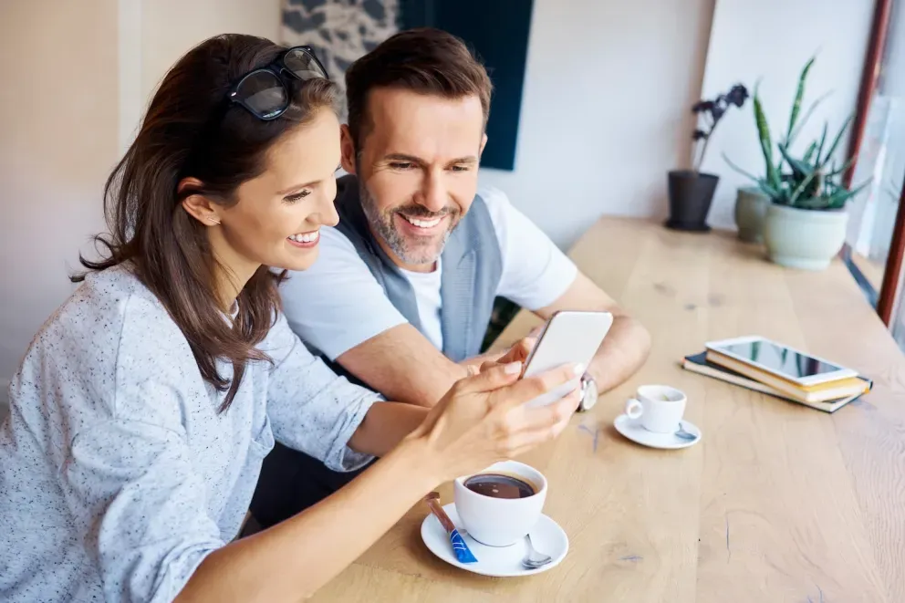 Hombre y mujer sonriendo mientras miran el teléfono