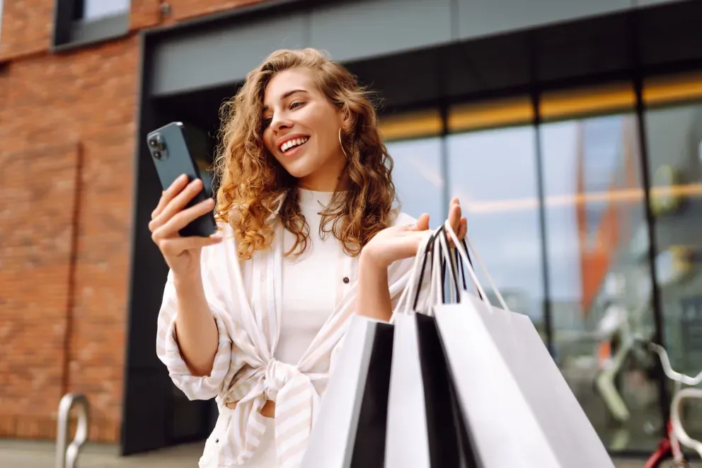 Mujer con teléfono y bolsas de la compra