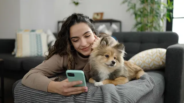 Mujer enviando mensajes de texto en su teléfono móvil acostada en el sofá con un perro