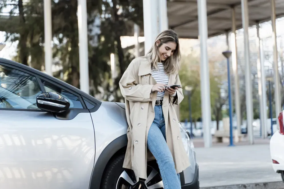Mujer joven feliz en el teléfono con el coche