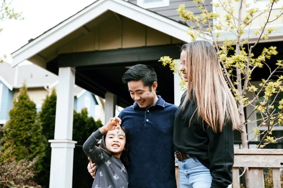 Una familia sonriente de tres personas de pie juntos al aire libre frente a una casa. Una familia sonriente de tres personas de pie juntos al aire libre frente a una casa.