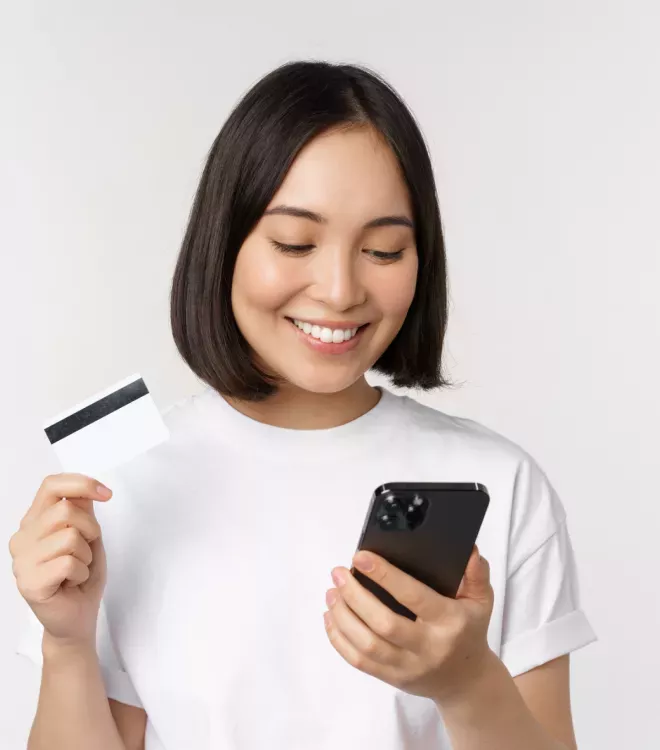 Mujer mirando un teléfono con una tarjeta de crédito