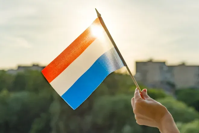 Hand holding Netherlands flag in sunset sky