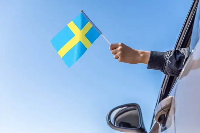 Hand holding Swedish flag outside of car